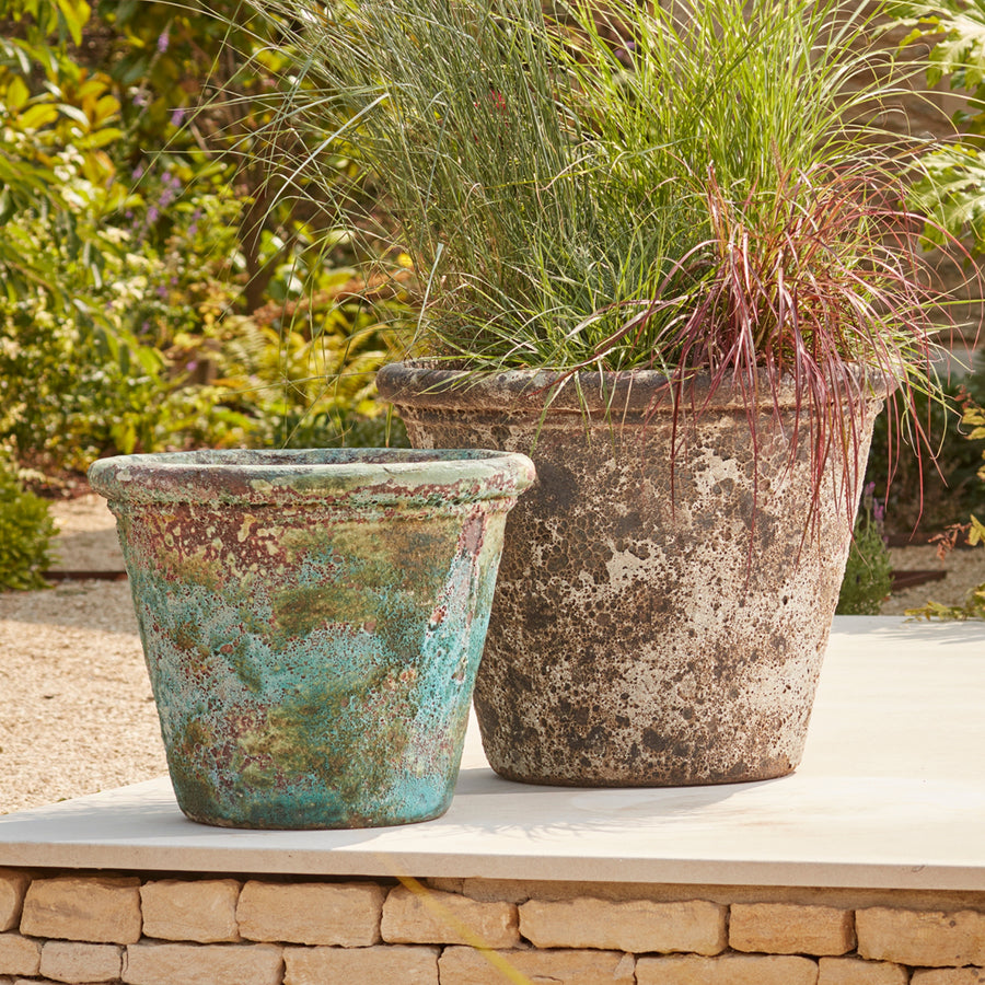 Ancient Glazed Stone Plant Pots in weathered turquoise and grey, styled with ornamental grasses on a modern patio for a Mediterranean-inspired garden look.