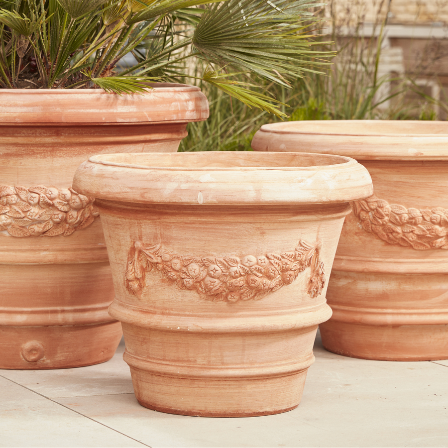  Large terracotta planters adorned with decorative floral carvings grace the paved surface, their earthy tones enhancing the surrounding greenery.