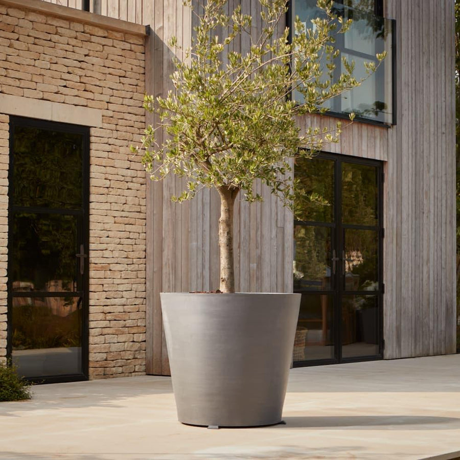 Tall contemporary metal planter with a sleek matte grey finish, styled with a tree on a modern patio for a minimalist outdoor aesthetic.