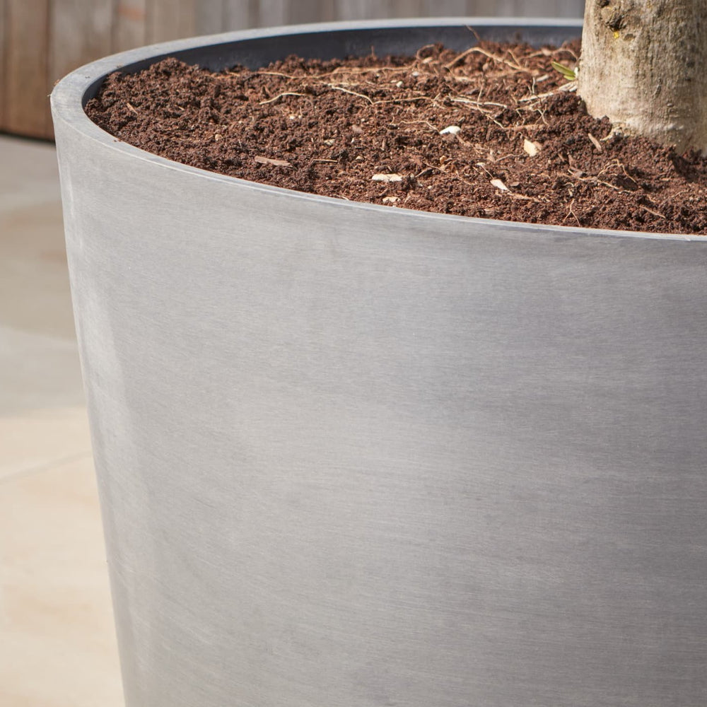 Tall contemporary metal planter filled with soil and a young tree, featuring a durable powder-coated finish for long-lasting outdoor use.