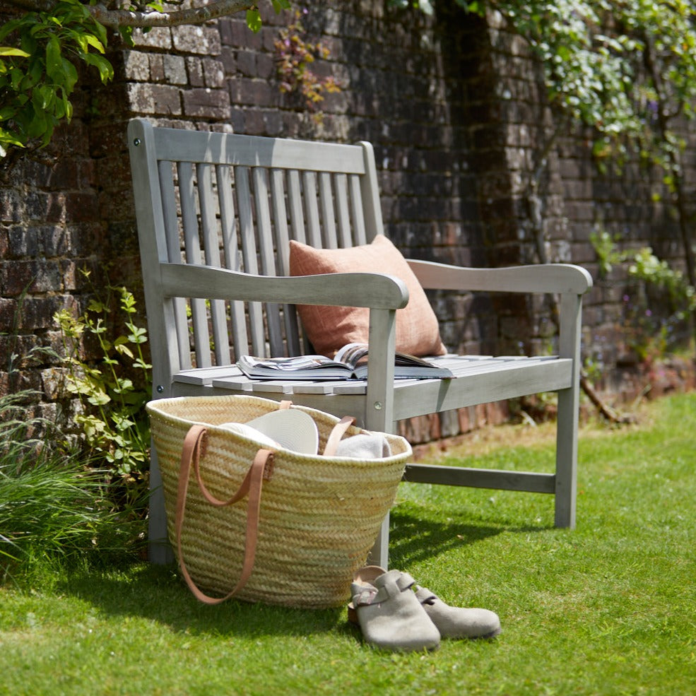 Repton Wooden Garden Bench styled in a cozy outdoor seating area, with a woven basket and soft cushions, creating an inviting spot for relaxation.