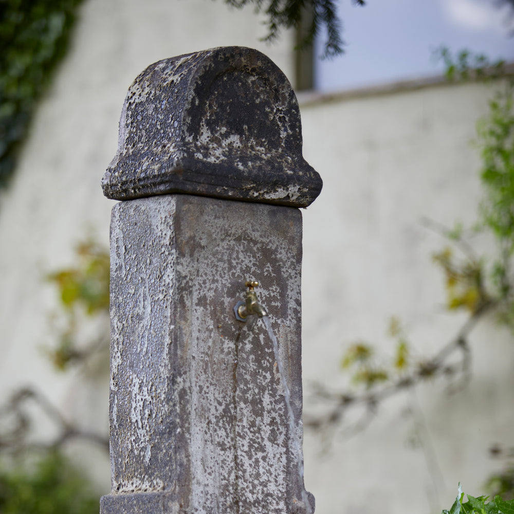 Detailed view of the ancient stone fountain’s textured patina and basin, showcasing its aged, rustic aesthetic.