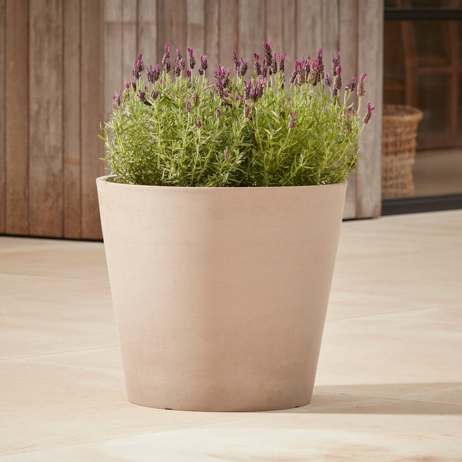 Gardenesque x EcoPots Round Plant Pot in taupe, featuring a sleek conical shape and hidden wheels, placed on a patio with lavender plants.