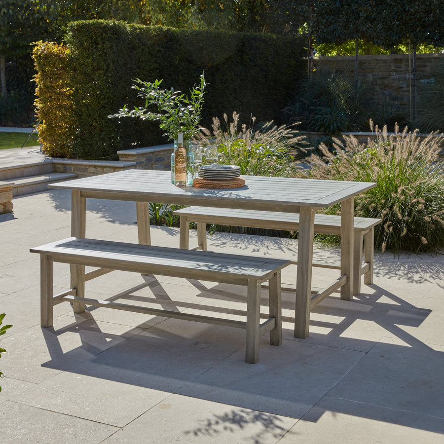 Wooden picnic-style outdoor dining set on a patio, styled for alfresco dining with tableware, plants, and a summer-ready setting.