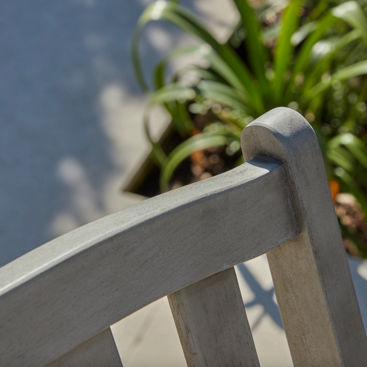 Close-up of the Repton Wooden Bistro Chair's curved backrest, highlighting its smooth, weathered grey finish and classic slatted design. Sunlight enhances the natural wood grain, showcasing the craftsmanship of this durable outdoor chair, perfect for garden, patio, and balcony seating.