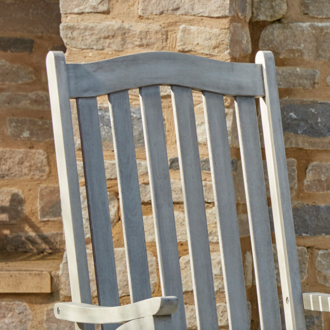 Close-up of the Repton Wooden Rocking Chair’s slatted backrest, highlighting its smooth curved top rail and weathered grey finish. Crafted for durability and comfort, this outdoor rocking chair is perfect for patios, porches, and garden relaxation. Set against a rustic brick wall for a classic aesthetic.