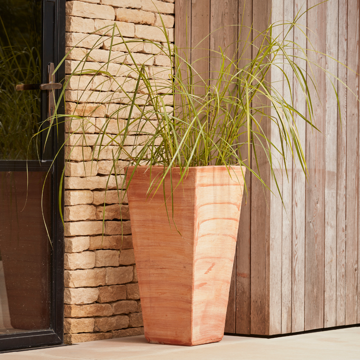 Sardinia Tall Square Tapered Terracotta Pot with a sleek, handcrafted finish, placed beside a modern entranceway and planted with ornamental grasses. A durable, frost-proof Italian terracotta planter designed for patios and courtyards.