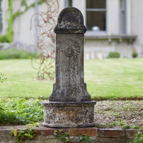 Ancient Stone Garden Water Fountain with a weathered finish, adding a timeless, rustic charm to a landscaped garden.