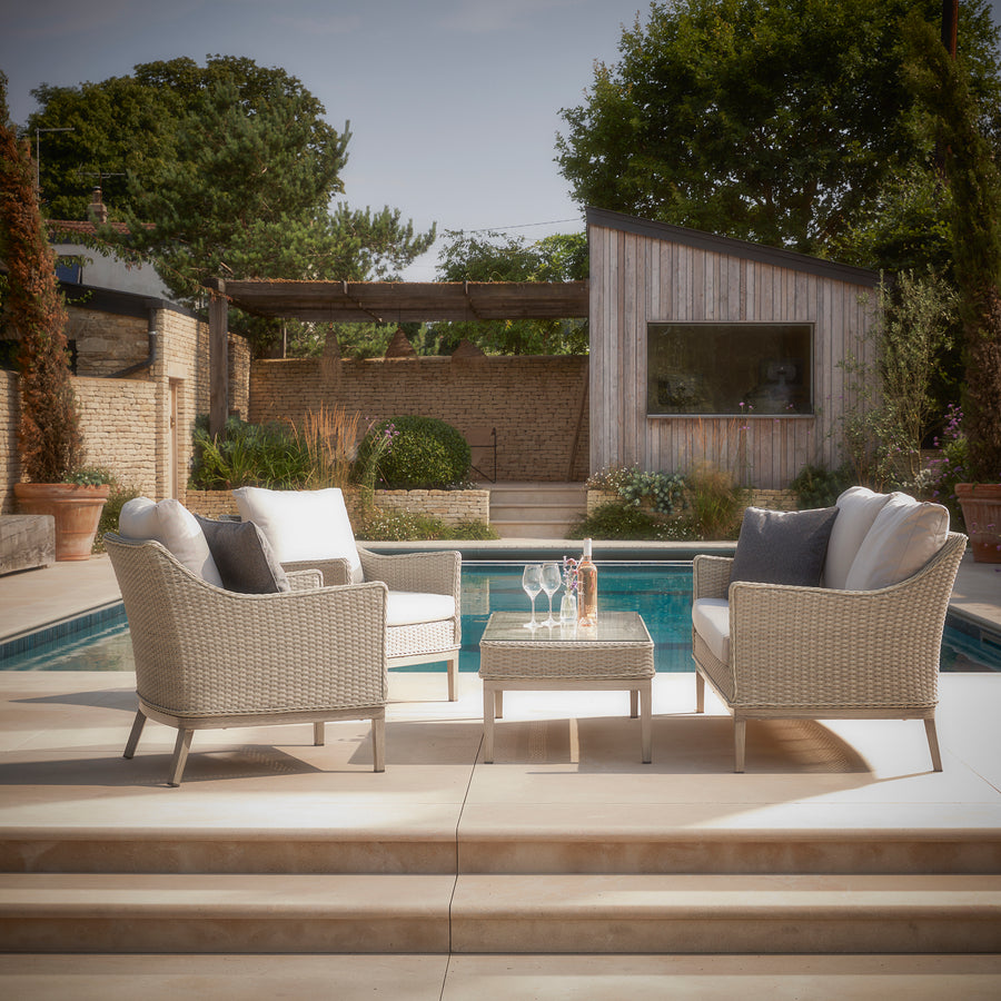 Paxton rattan lounge set styled by a poolside, featuring two cushioned armchairs, a matching coffee table, and a contemporary woven rattan design.