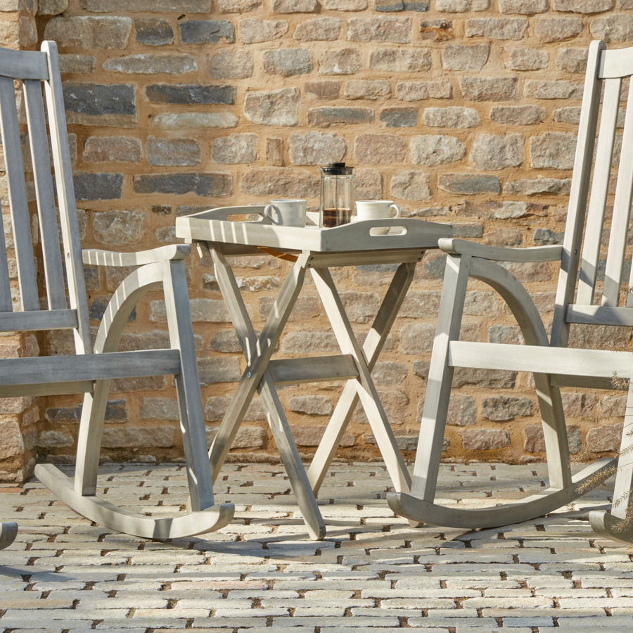 Repton outdoor wooden tray table in a grey wash finish, styled on a patio between two Repton rocking chairs for an elegant garden setup.