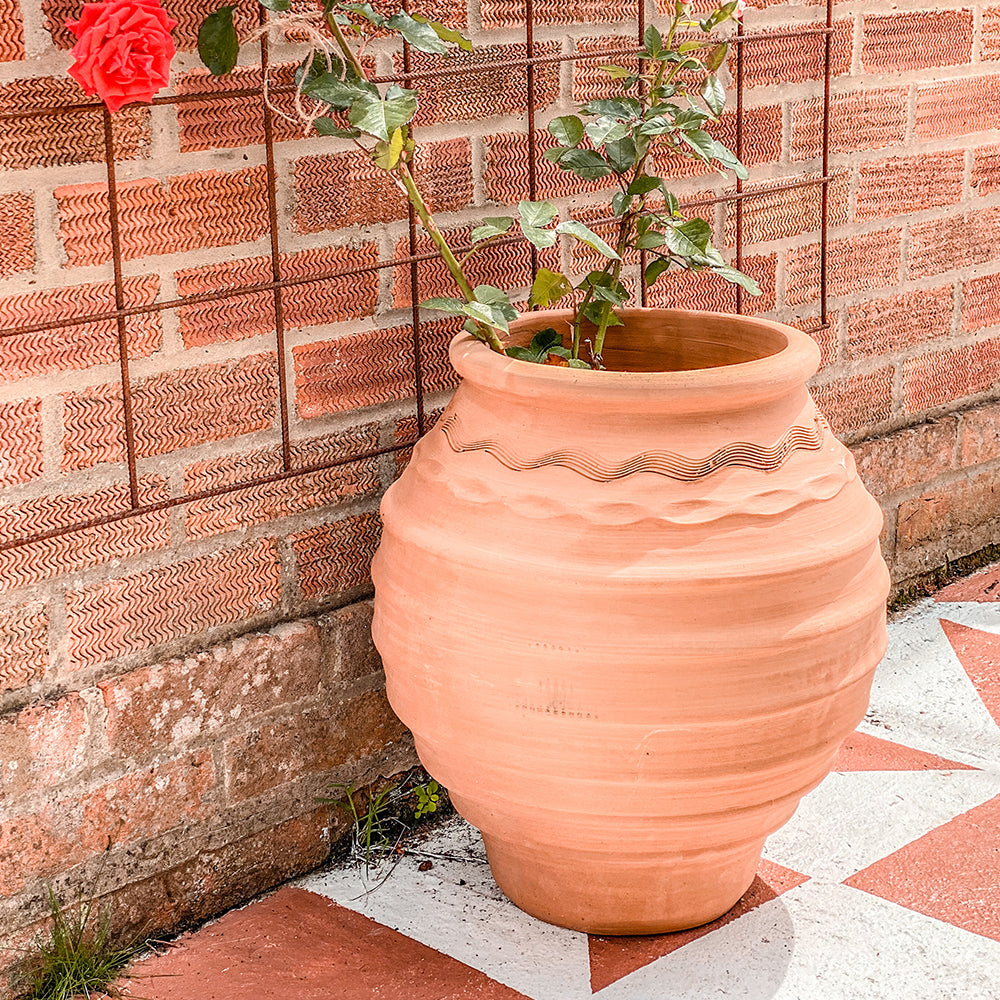 A pair of Grecian terracotta planters of different sizes, positioned on a tiled outdoor patio with a textured brick background.