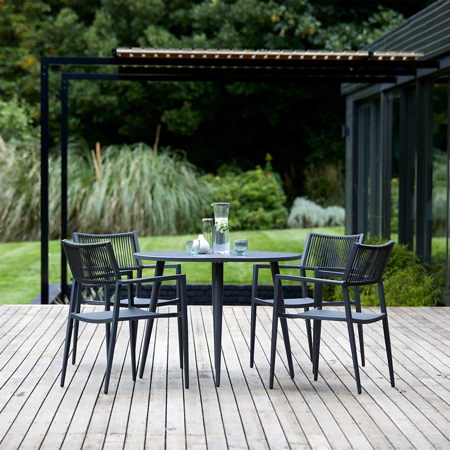 A modern 4-seater garden dining set on a wooden deck, featuring a round table and black weave-twist chairs, perfect for alfresco dining.