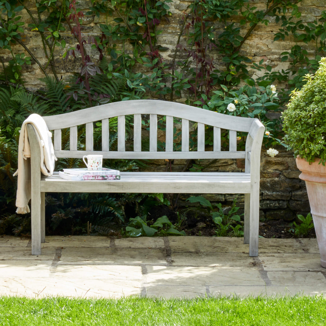 Repton Queen Wooden Garden Bench in a neutral finish, styled in a sunlit courtyard with a throw draped over the armrest.