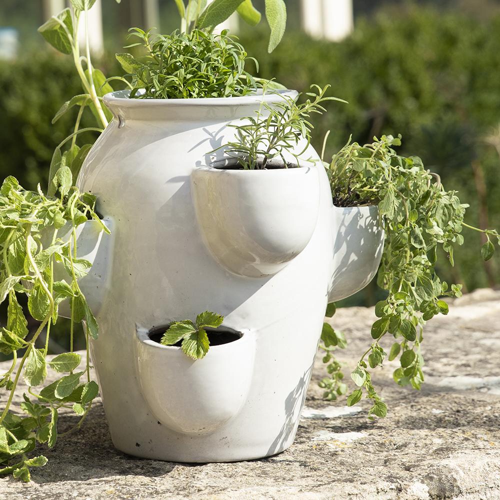 A tiered ceramic herb planter with multiple planting pockets, placed on a stone surface and filled with fresh herbs.